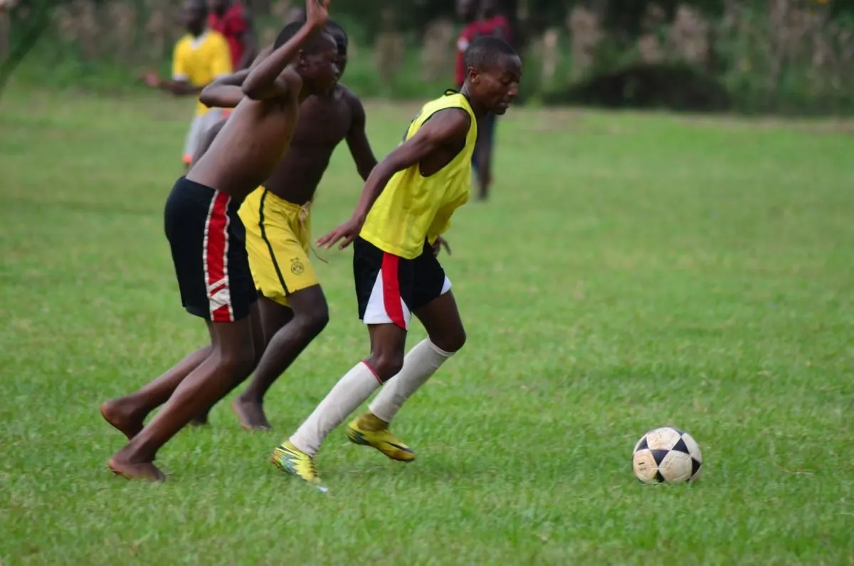 Players chase the ball on a grass pitch.